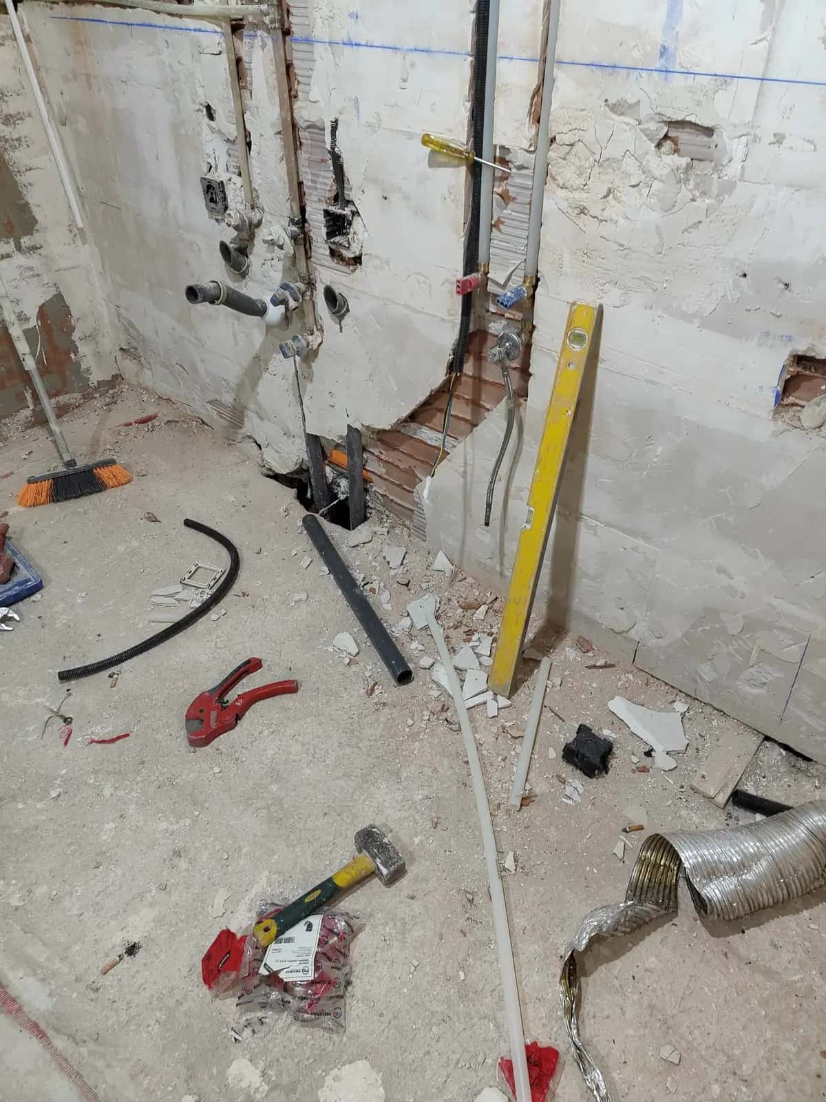 Baño en demolición con tomas de agua, tubos y herramientas repartidas por el suelo