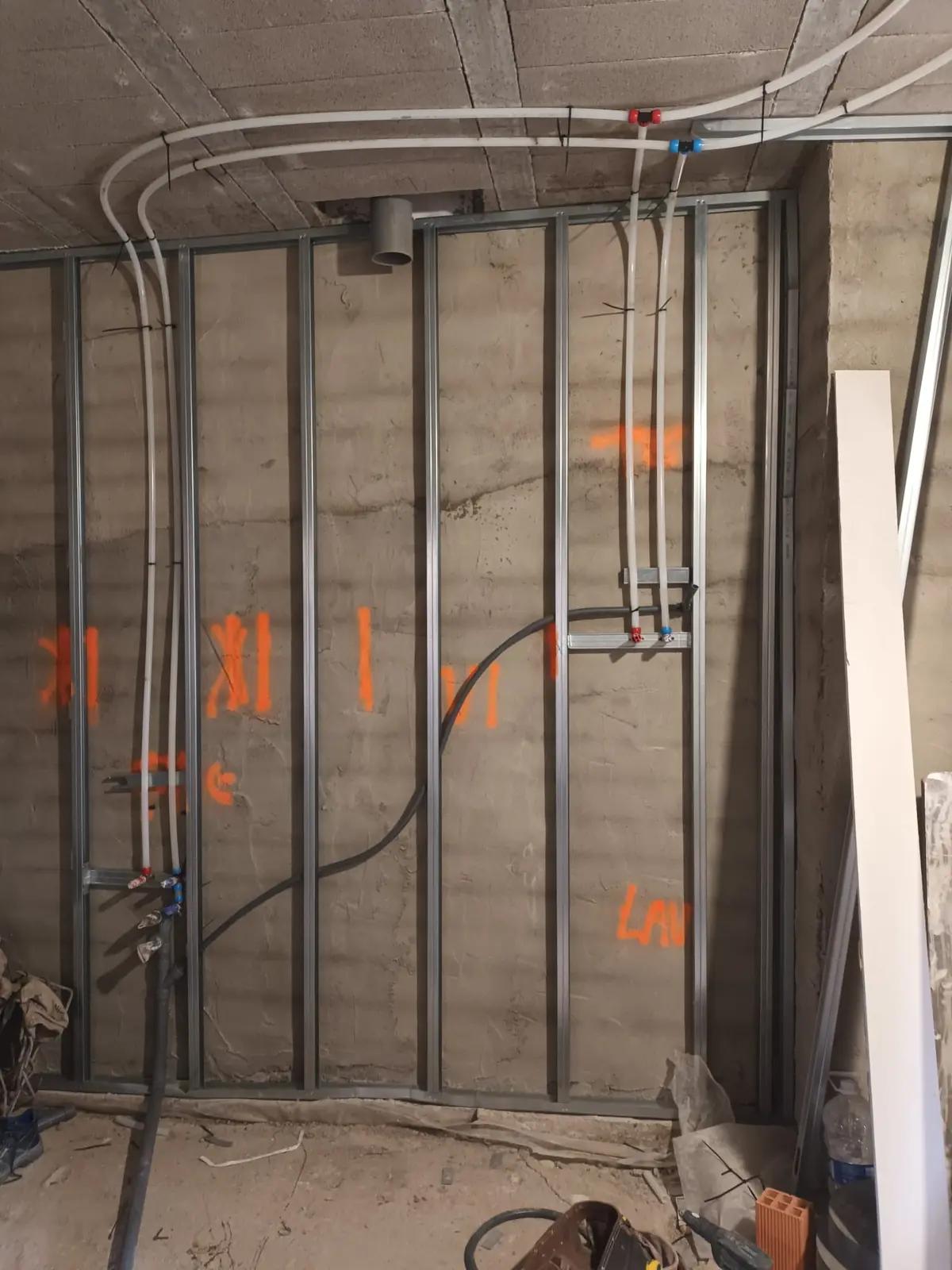 Tabique de perfiles metálicos con tuberías multicapa y marcas de replanteo en la pared